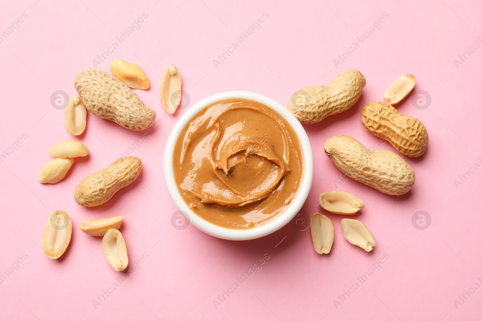 Photo of Tasty peanut butter in bowl and groundnuts on pink table, flat lay