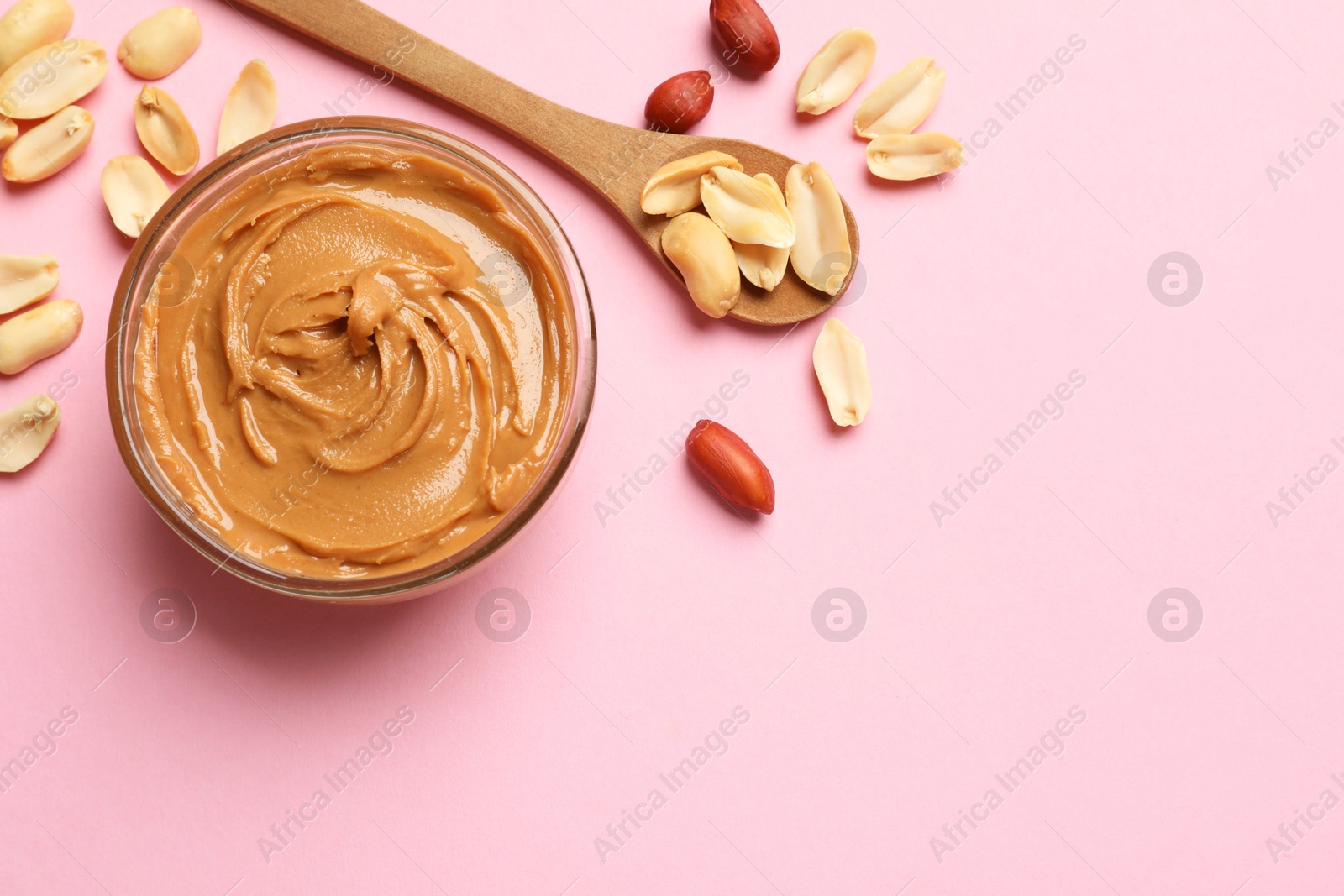 Photo of Tasty peanut butter in bowl and spoon with groundnuts on pink table, flat lay. Space for text