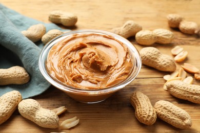 Photo of Tasty peanut butter in bowl and groundnuts on wooden table