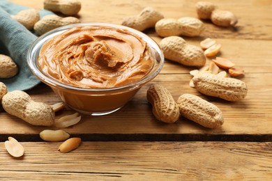 Tasty peanut butter in bowl and groundnuts on wooden table