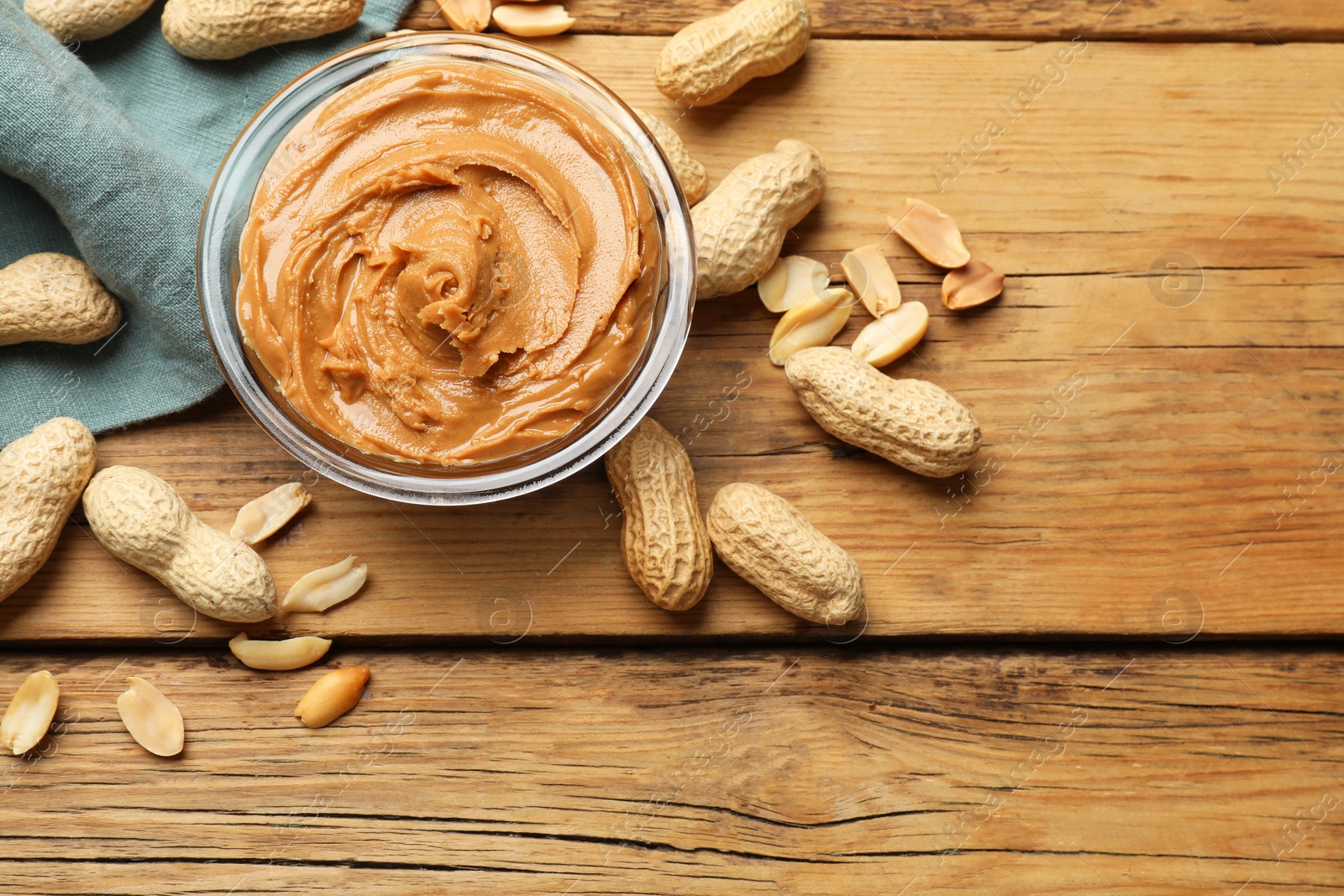 Photo of Tasty peanut butter in bowl and groundnuts on wooden table, flat lay. Space for text