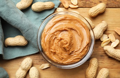 Photo of Tasty peanut butter in bowl and groundnuts on wooden table, flat lay