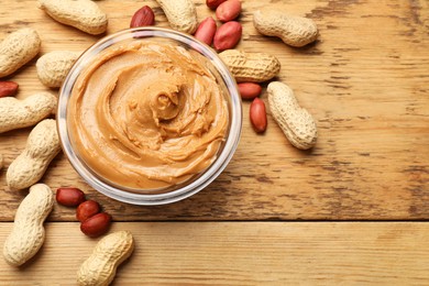 Photo of Tasty peanut butter in bowl and groundnuts on wooden table, flat lay. Space for text