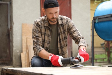 Man polishing wooden planks with angle grinder outdoors