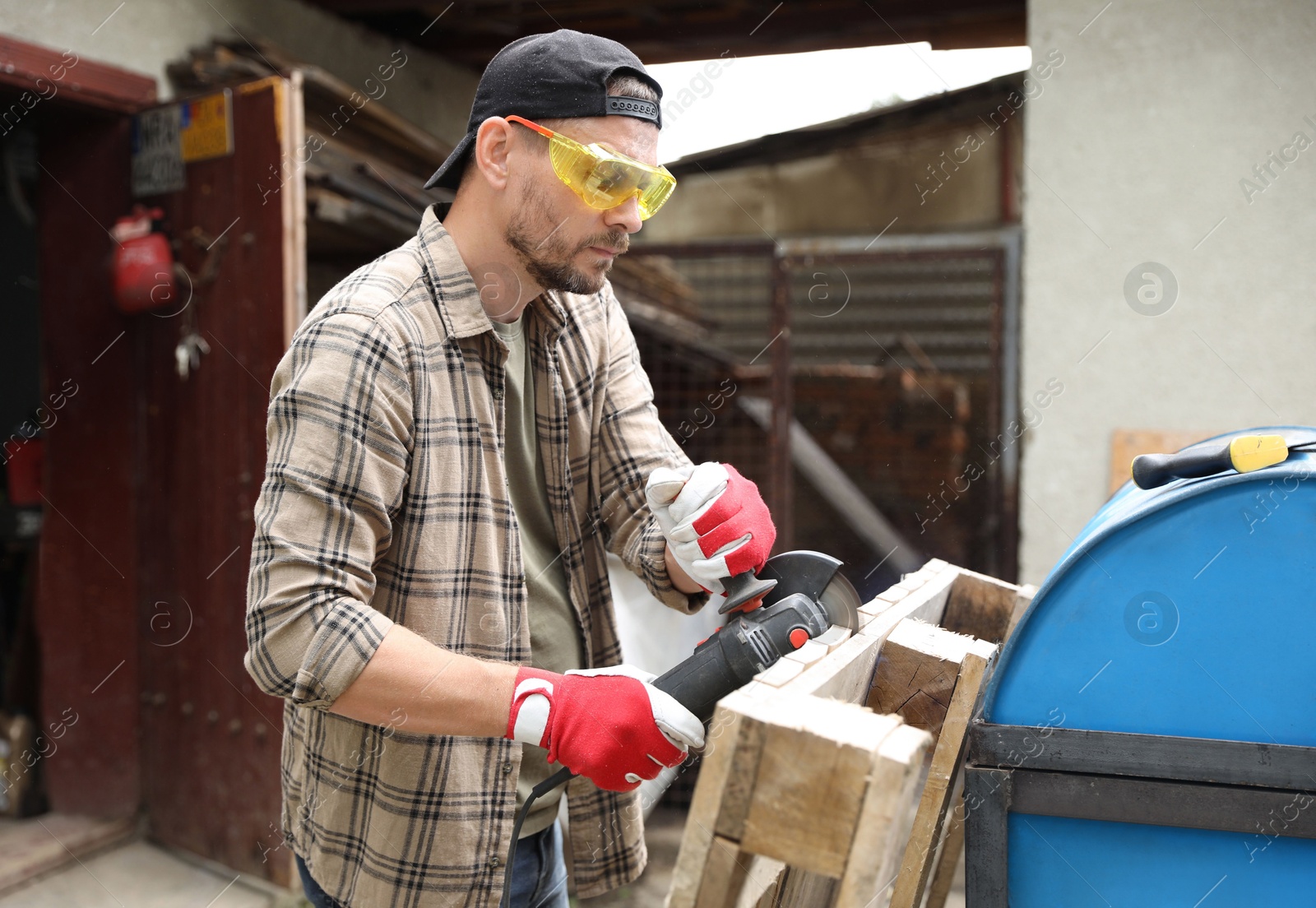 Photo of Man grinding wooden planks with angle grinder outdoors