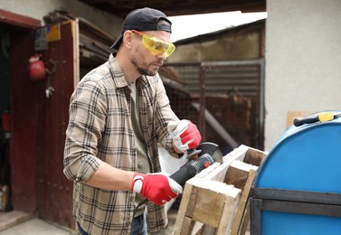 Photo of Man grinding wooden planks with angle grinder outdoors