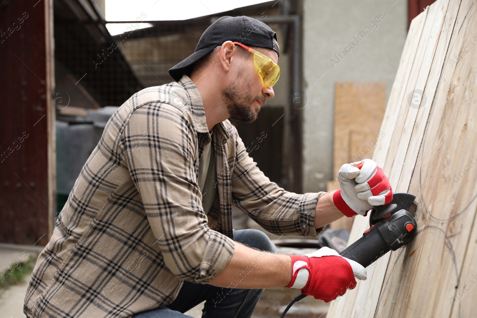 Photo of Man grinding wooden planks with angle grinder outdoors