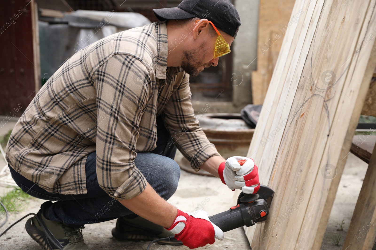 Photo of Man grinding wooden planks with angle grinder outdoors