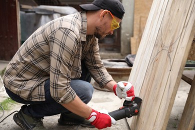 Photo of Man grinding wooden planks with angle grinder outdoors