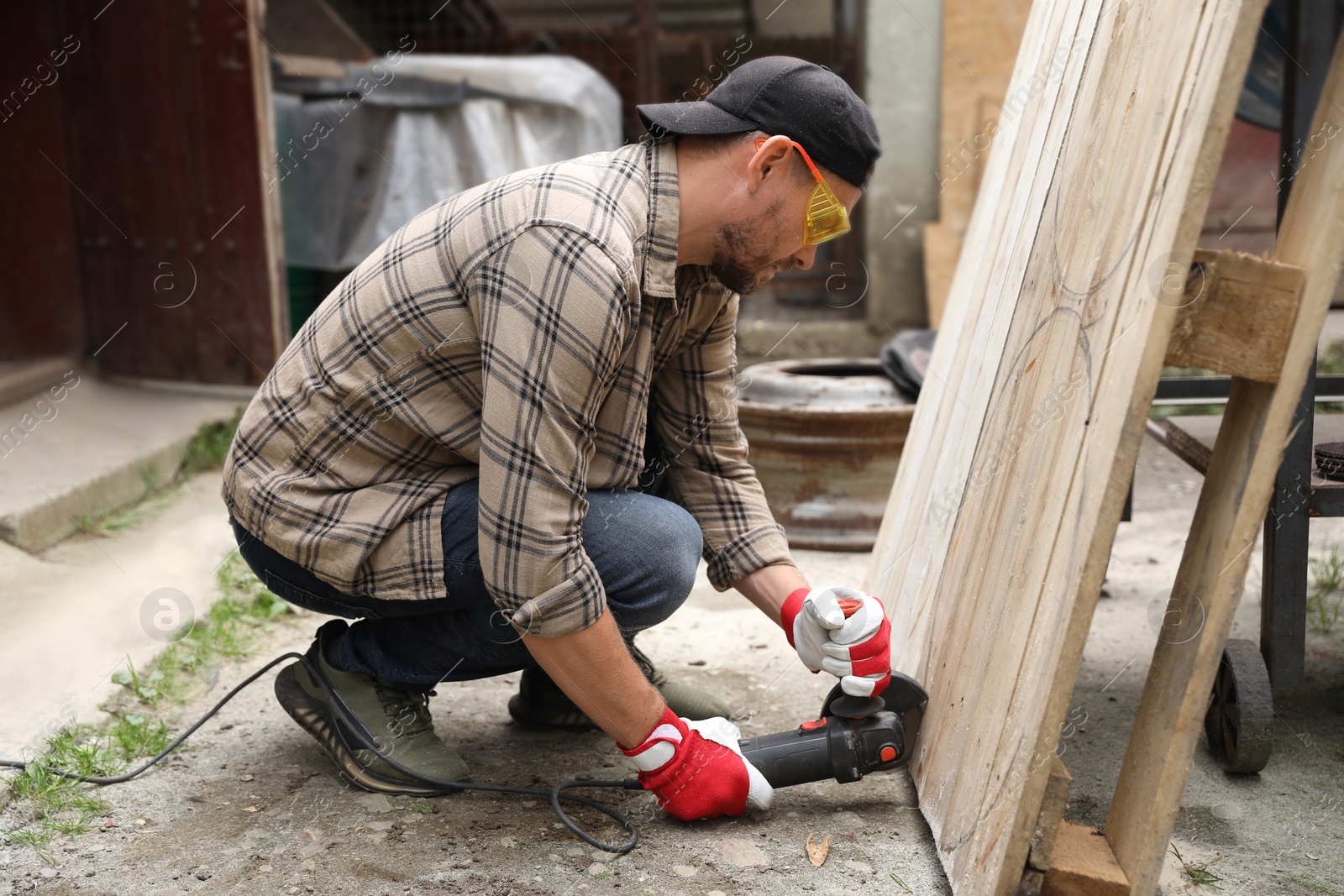 Photo of Man grinding wooden planks with angle grinder outdoors