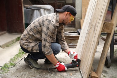 Photo of Man grinding wooden planks with angle grinder outdoors