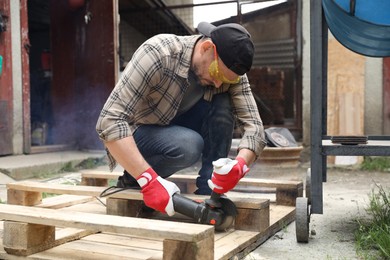 Photo of Man grinding wooden planks with angle grinder outdoors