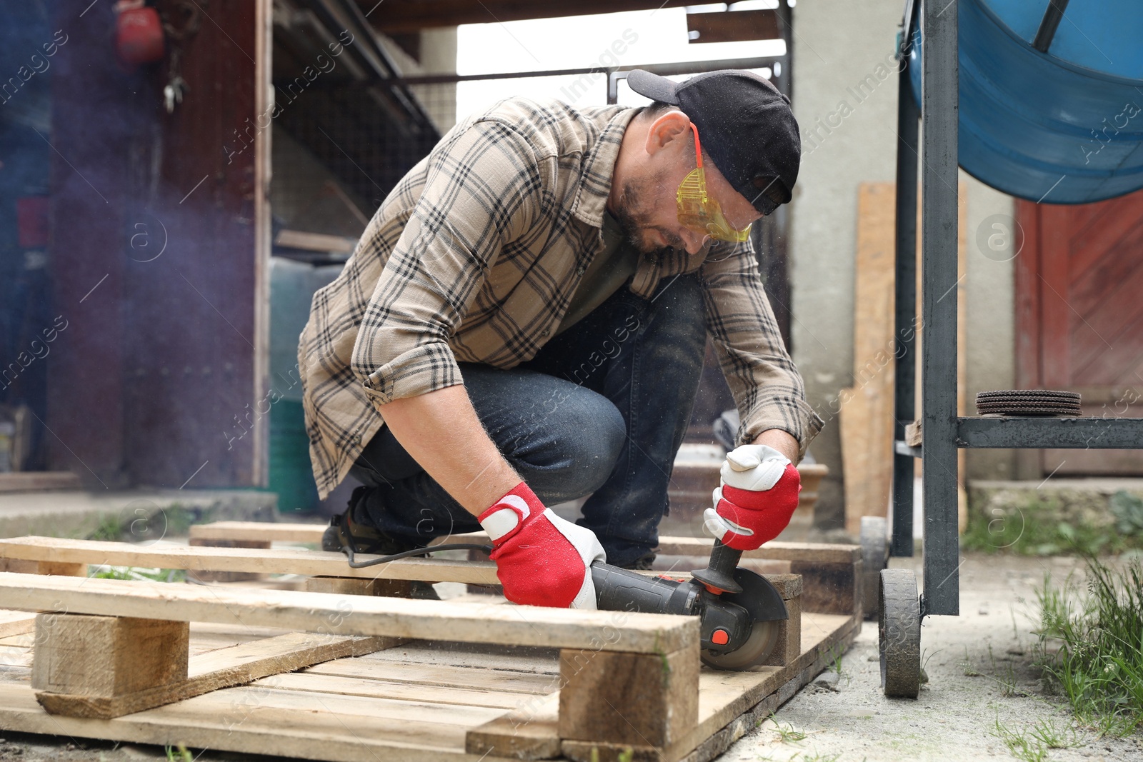 Photo of Man grinding wooden planks with angle grinder outdoors