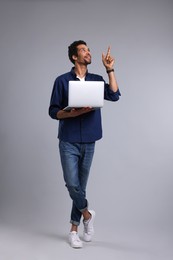 Happy man with laptop pointing at something on grey background