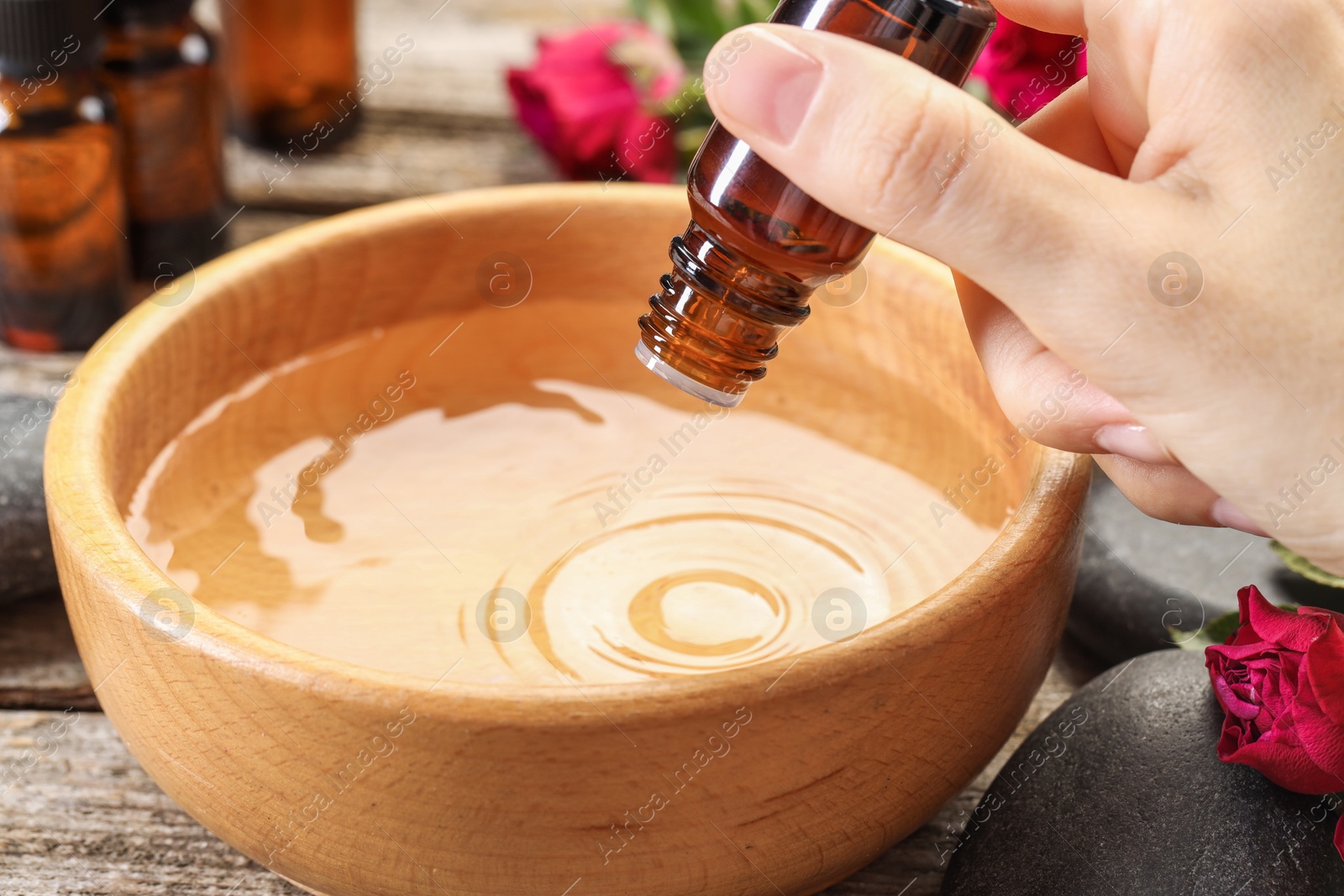 Photo of Woman dripping essential oil into bowl with water at wooden table, closeup