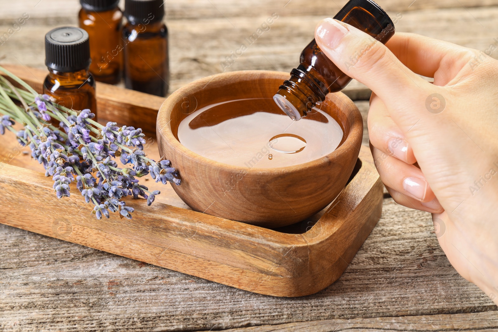 Photo of Woman dripping essential oil into bowl with water at wooden table, closeup