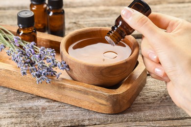 Woman dripping essential oil into bowl with water at wooden table, closeup