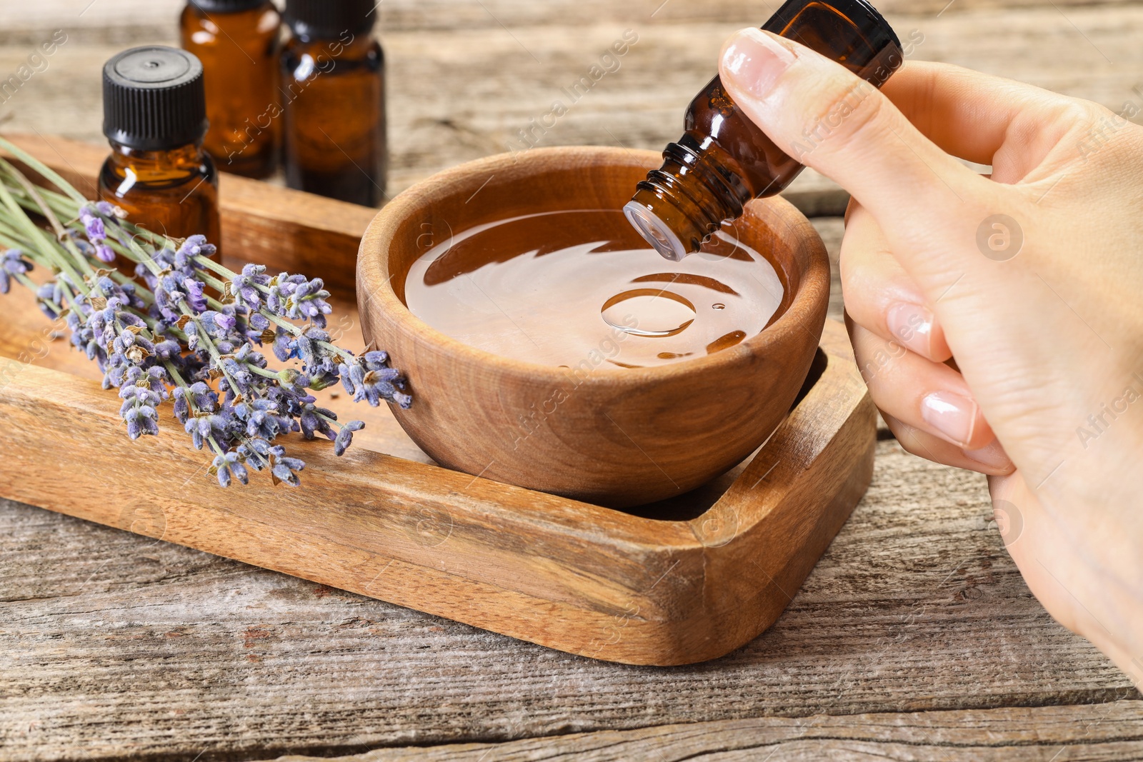 Photo of Woman dripping essential oil into bowl with water at wooden table, closeup