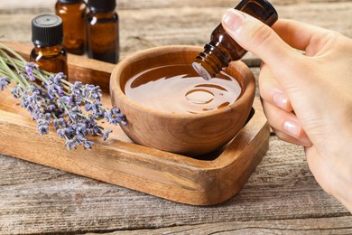 Photo of Woman dripping essential oil into bowl with water at wooden table, closeup