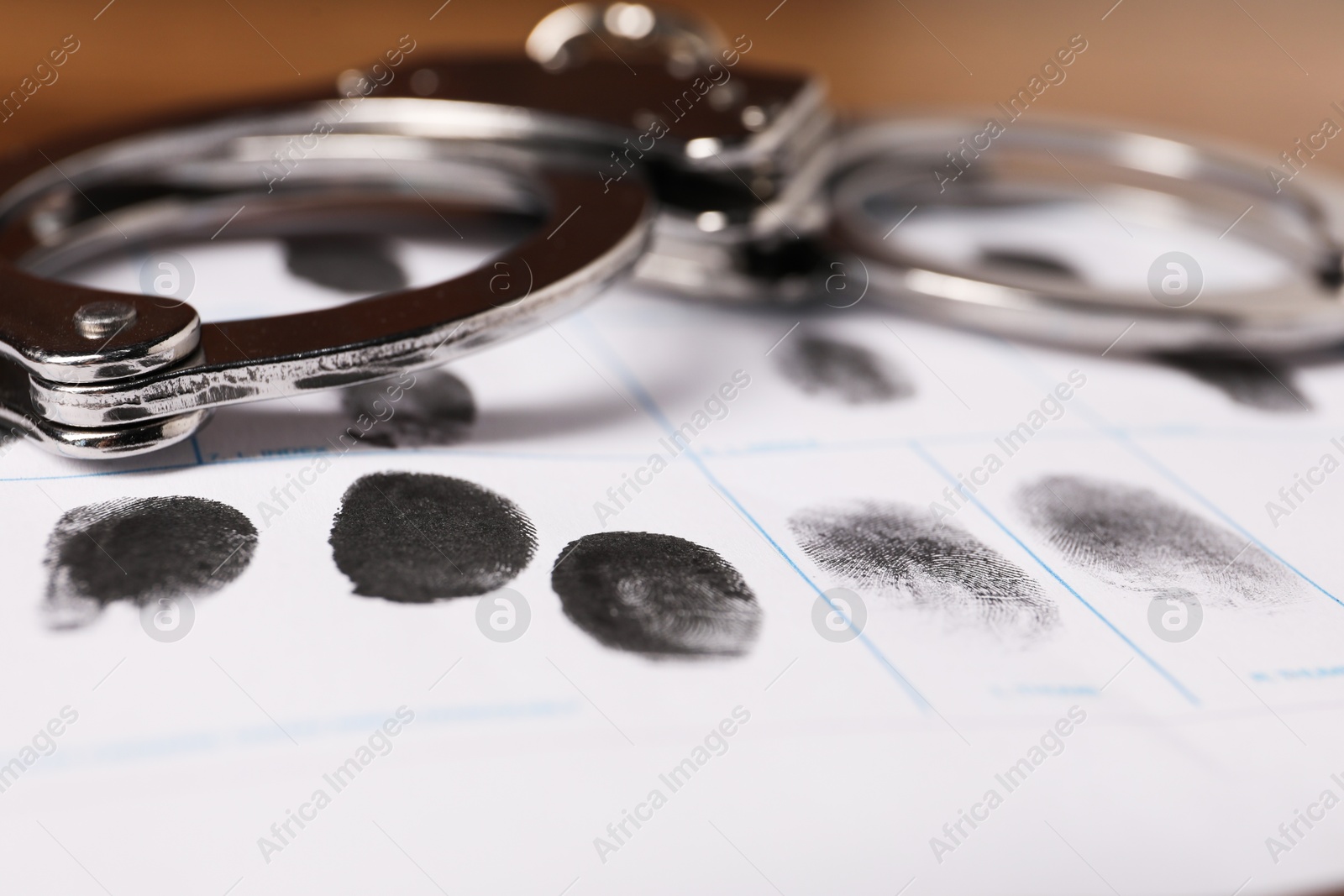 Photo of Paper sheet with human fingerprints and handcuffs on table, closeup. Criminal conviction