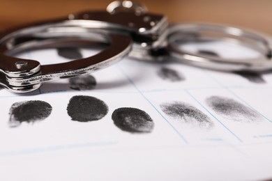 Paper sheet with human fingerprints and handcuffs on table, closeup. Criminal conviction