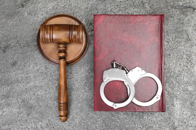 Book, judge's gavel and handcuffs on gray textured table, flat lay