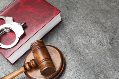 Photo of Book, judge's gavel and handcuffs on gray textured table. Space for text