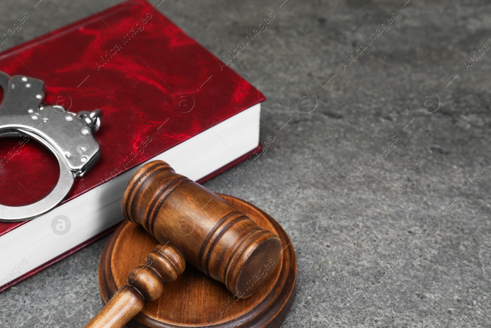 Photo of Book, judge's gavel and handcuffs on gray textured table, closeup. Space for text