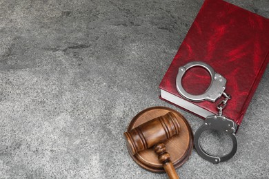 Book, judge's gavel and handcuffs on gray textured table, above view. Space for text