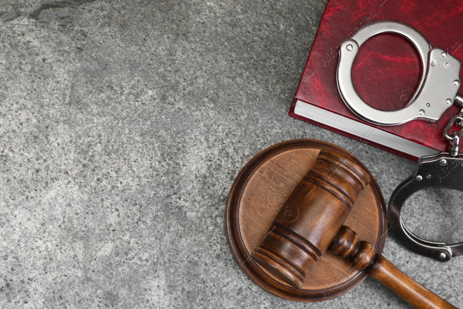 Photo of Book, judge's gavel and handcuffs on gray textured table, flat lay. Space for text