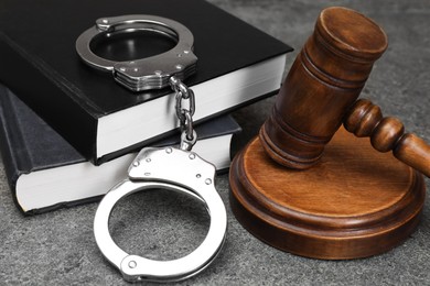 Books, judge's gavel and handcuffs on gray textured table, closeup