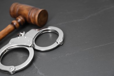 Photo of Judge's gavel and handcuffs on gray textured table, closeup. Space for text