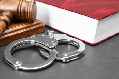 Book, judge's gavel and handcuffs on gray textured table, closeup