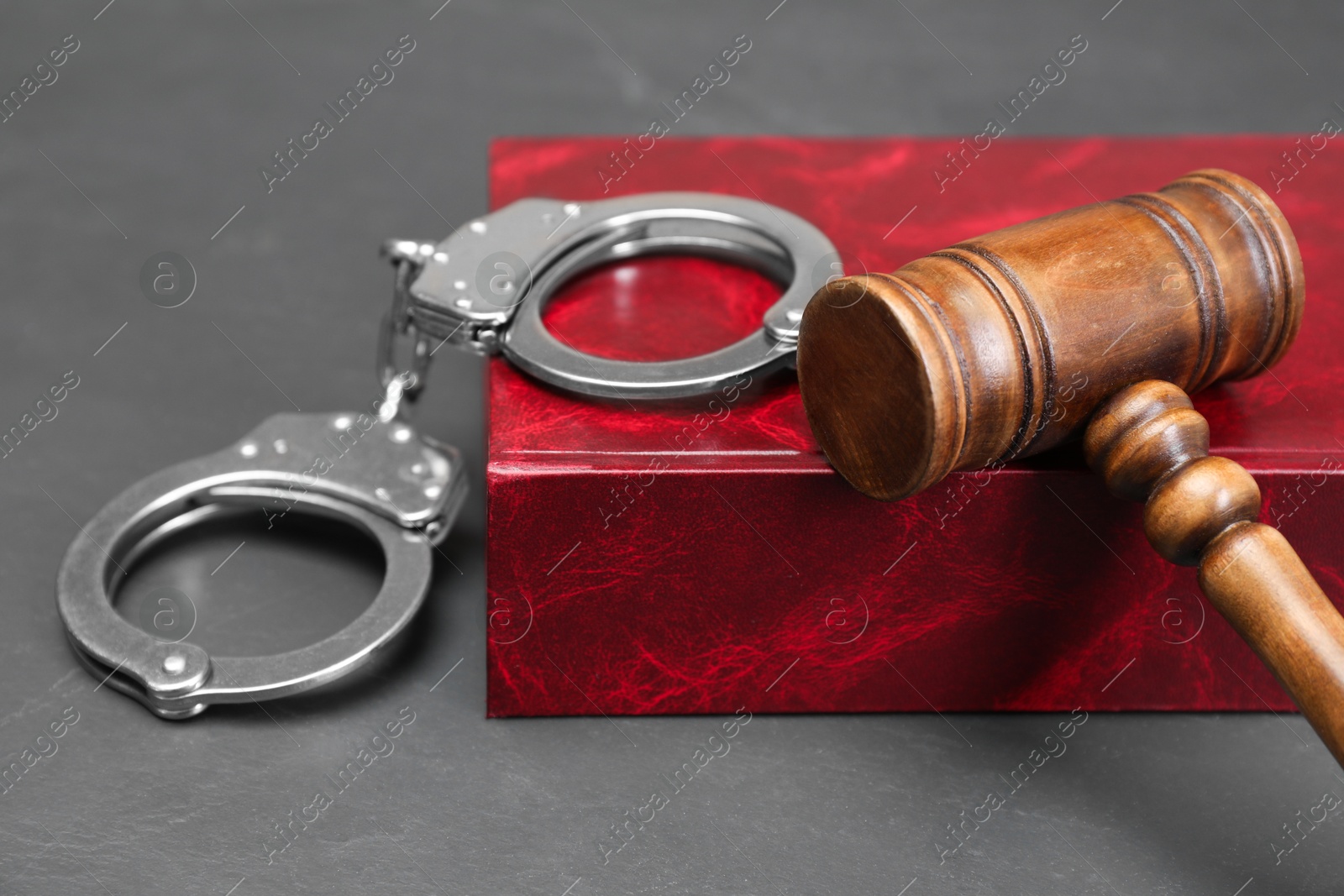 Photo of Book, judge's gavel and handcuffs on gray textured table, closeup