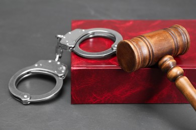 Book, judge's gavel and handcuffs on gray textured table, closeup