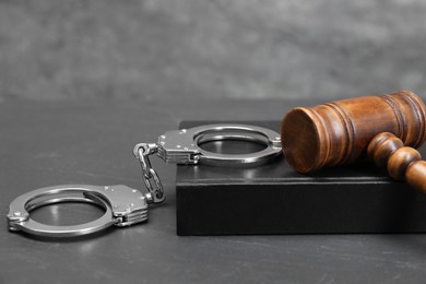 Book, judge's gavel and handcuffs on gray textured table, closeup