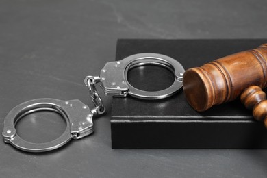 Book, judge's gavel and handcuffs on gray textured table, closeup