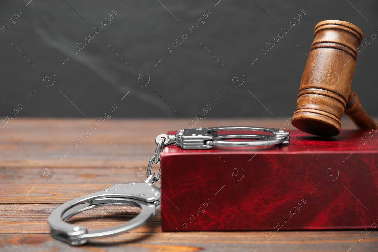 Photo of Book, judge's gavel and handcuffs on wooden table against gray background, space for text