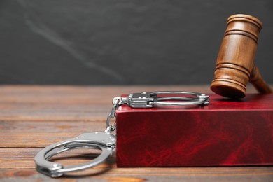 Book, judge's gavel and handcuffs on wooden table against gray background, space for text