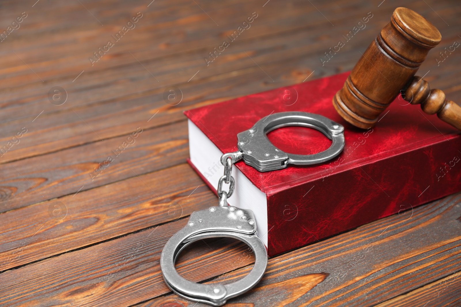 Photo of Book, judge's gavel and handcuffs on wooden table, closeup. Space for text