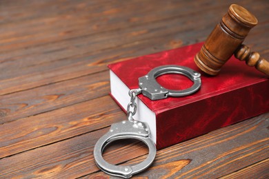 Photo of Book, judge's gavel and handcuffs on wooden table, closeup. Space for text