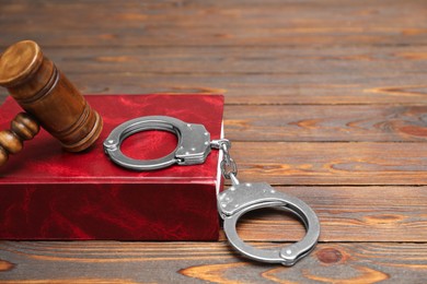 Photo of Book, judge's gavel and handcuffs on wooden table, closeup. Space for text