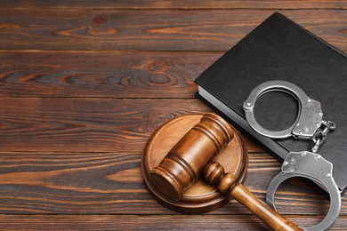 Photo of Book, judge's gavel and handcuffs on wooden table. Space for text