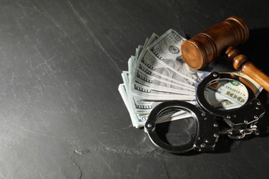 Handcuffs with dollar banknotes and wooden gavel on grey textured table. Space for text