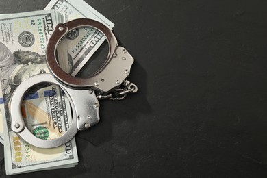 Photo of Handcuffs with dollar banknotes on grey textured table, flat lay. Space for text