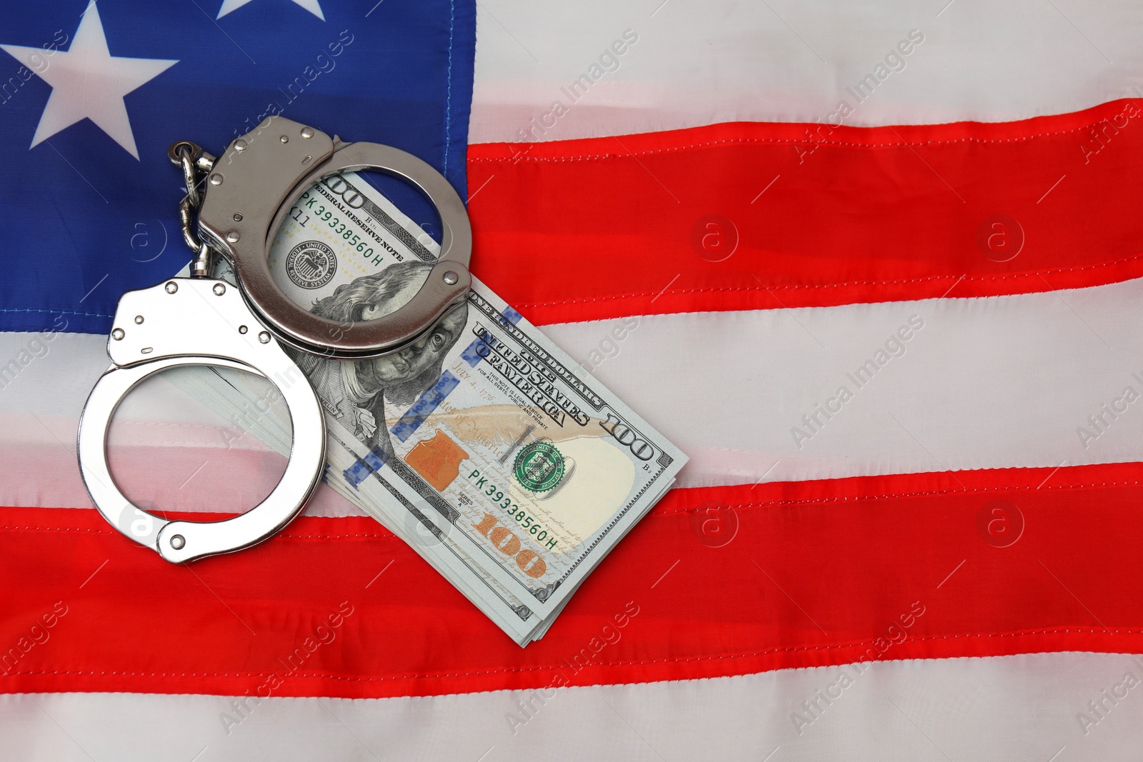 Photo of Handcuffs with dollar banknotes on American flag, flat lay. Space for text