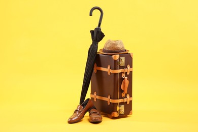 Photo of Brown suitcase, shoes, hat and umbrella on yellow background