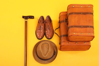 Photo of Suitcases, shoes, hat and cane on yellow background, above view