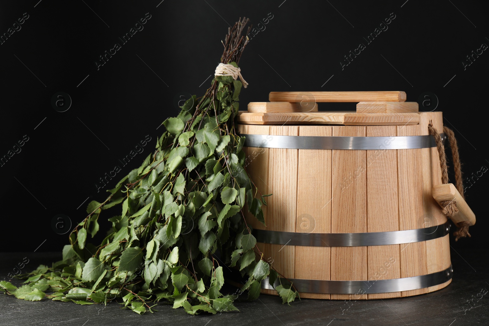 Photo of Sauna equipment. Bucket and birch whisk on black textured surface