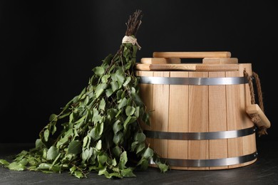 Sauna equipment. Bucket and birch whisk on black textured surface